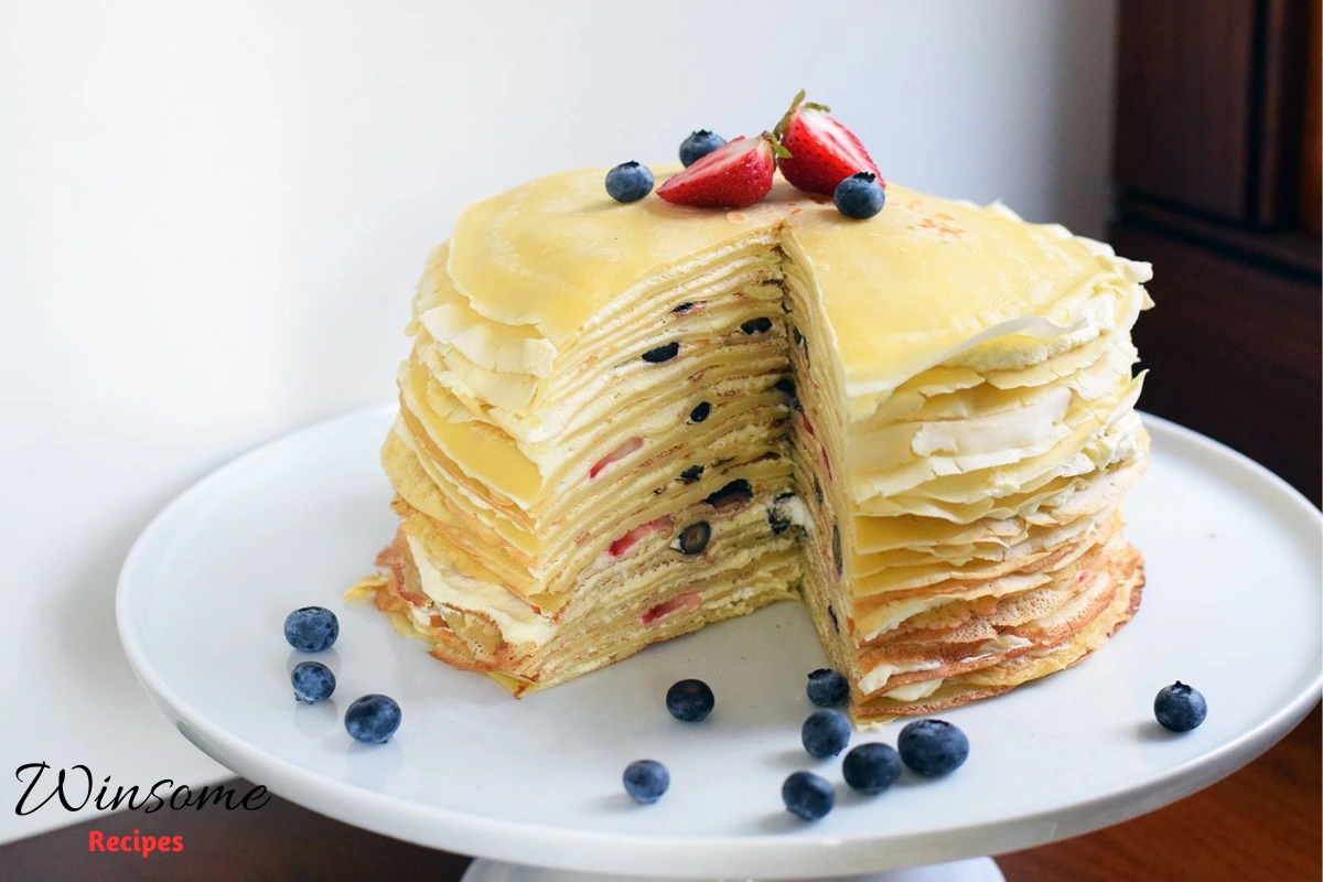 A beautifully layered crepe cake on a rustic wooden table, showcasing delicate, thin crepes stacked high with creamy filling in between each layer - winsome recipes