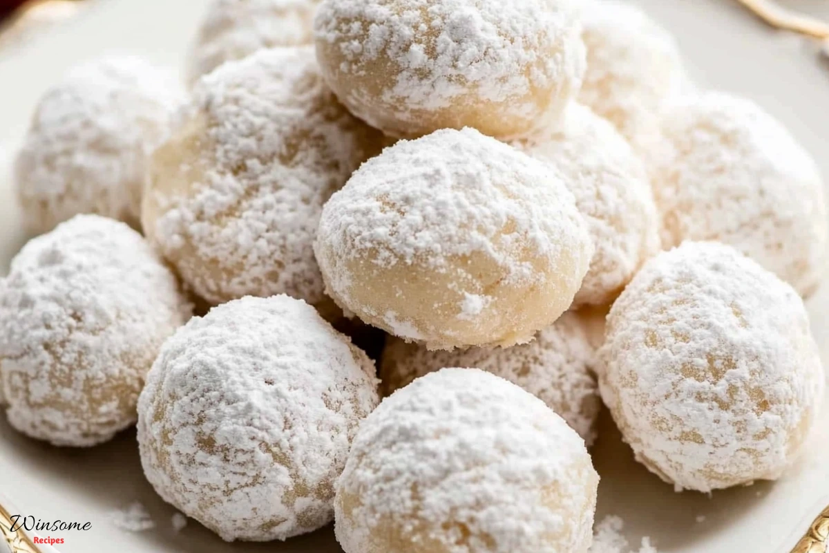 A plate of snowball cookies dusted with powdered sugar, beautifully arranged on a wooden table.