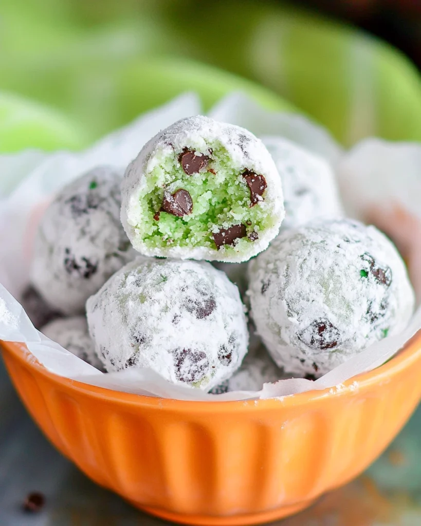 A bowl of Mint Chocolate Chip Snowball Cookies, featuring chocolate chips and vibrant green candy pieces.