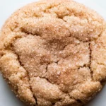 A delicious sugar cookie topped with cinnamon sticks, resting on a clean white surface, perfect for a snickerdoodle treat.