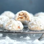 A plate of snowball cookies with pecans dusted with powdered sugar and sprinkled with pecans, inviting and delicious.